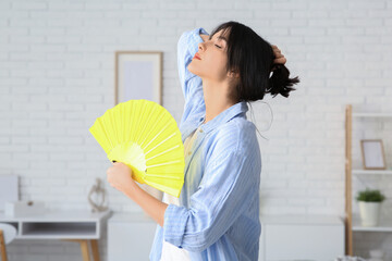 Young pretty woman with hand fan suffering from heat in room