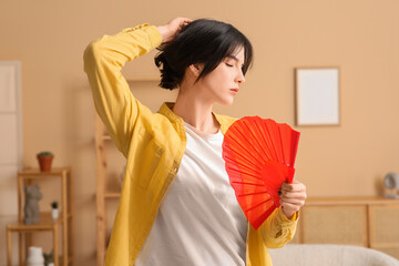 Young woman with hand fan suffering from heat in room