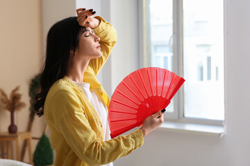 Young woman with hand fan suffering from heat in room