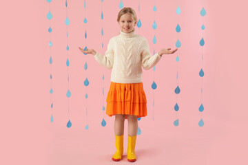 Adorable girl in rubber boots with paper raindrops on pink background
