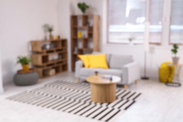 Modern interior of light living room with cozy sofa, shelving units, houseplants and coffee table, blurred view