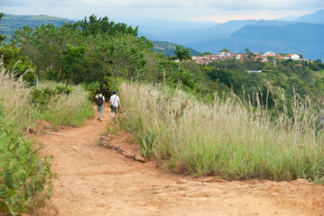 Pair of unrecognizable travelers seen from behind walking along a dirt road in a natural tourist...