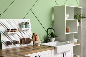 Pegboard, white counters and rack near green wall in interior of modern kitchen