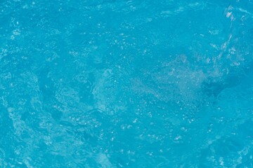 Blue water with ripples on the surface. Defocus blurred transparent blue colored clear calm water surface texture with splashes and bubbles. Water waves with shining pattern texture background.