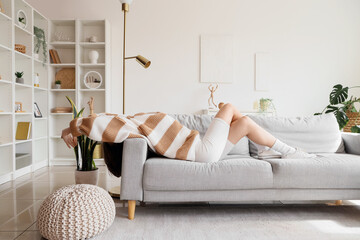 Young happy woman relaxing on cozy sofa in light living room
