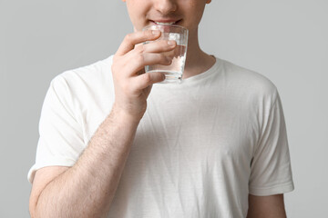 Young man drinking clean water on grey background