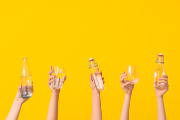 Female hands with bottles and glasses of water on yellow background