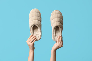 Female hands holding pair of slippers on blue background