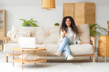 Young African-American woman on sofa watching TV at home