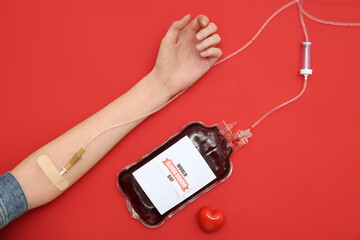 Female hand with blood pack for transfusion with text WORLD BLOOD DONOR DAY and heart-shaped grip...