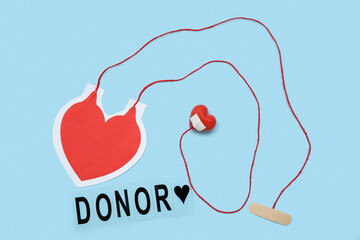 Composition with paper heart-shaped blood pack for transfusion, letters DONOR and grip ball on blue...