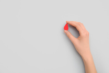 Female hand with paper blood drop on grey background. Donation blood concept.