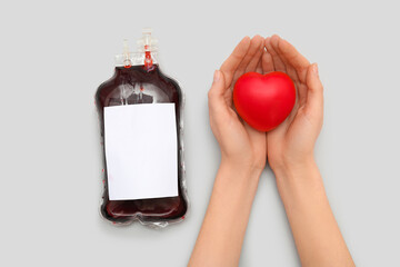 Female hands with heart and blood pack for transfusion on grey background
