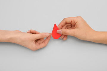 Female hands with paper blood drop on grey background. Donation blood concept.