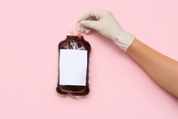 Female hand in rubber glove holding blood pack for transfusion on pink background