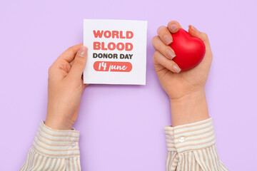 Female hands holding with grip ball and paper sheet with text WORLD BLOOD DONOR DAY 14 JUNE on lilac background