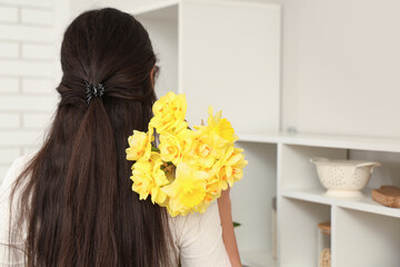 Beautiful young woman with narcissus bouquet at home, back view