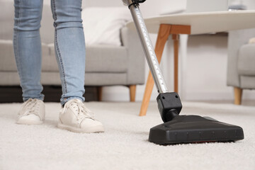 Young woman cleaning carpet with cordless stick vacuum cleaner in living room, closeup