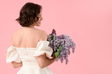 Young woman with bouquet of blooming lilac flowers on pink background, back view