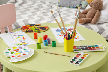 Paints with paper sheets on table in children's bedroom, closeup
