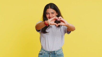 Woman in love. Smiling attractive Indian woman makes heart gesture demonstrates love sign expresses good positive feelings and sympathy. Arabian Hindu young girl isolated on yellow wall background