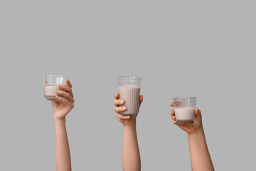 Female hands with glasses of sweet chocolate milk on grey background