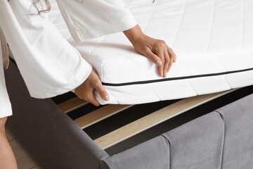 Young woman putting soft mattress on bed at home, closeup