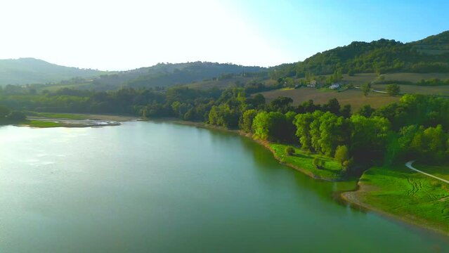 Rapid aerial pullback and pan-left shot from Lago di San Ruffino, an overarching vision ranging from the vegetation-filled shores to the pristine lake waters shining with sun glare amongst mountains