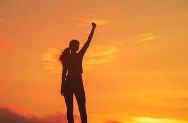 Empowered woman raising arm in celebration at sunset