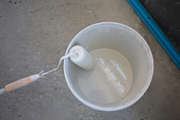 The paint roller is placed on the edge of the paint bucket.