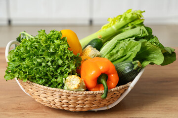 Wicker basket with different fresh vegetables on wooden kitchen counter