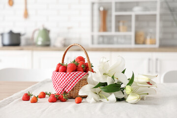 Wicker basket with tasty strawberries and lily flowers on table in kitchen
