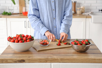 Woman cutting tasty strawberries on table in kitchen