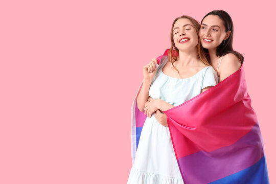 Beautiful young lesbian couple with Bisexual flag hugging on pink background