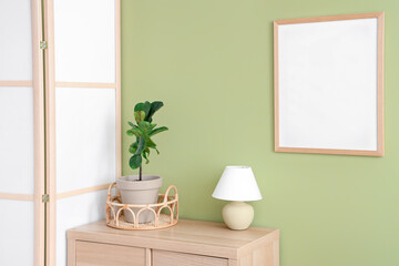 Interior of room with folding screen, commode and houseplant near green wall