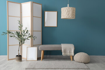 Interior of room with folding screen, bench and houseplant near blue wall