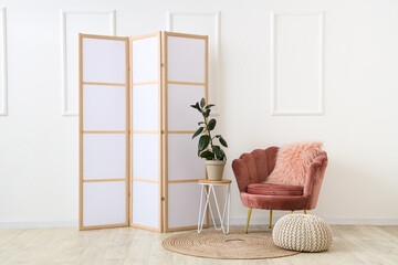 Interior of room with folding screen, houseplant and armchair near white wall