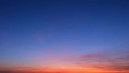 A beautiful gradient sky transitioning from deep blue at the top to vibrant orange and pink hues near the horizon. This serene sunrise showcases a peaceful dawn. Sunrise sky background.

