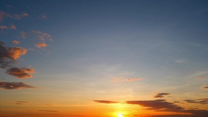 A serene sunrise with the sun partially visible on the horizon. The sky transitions from deep blue to warm orange and yellow hues. Sparse clouds are tinged with orange light. Cloud background.
