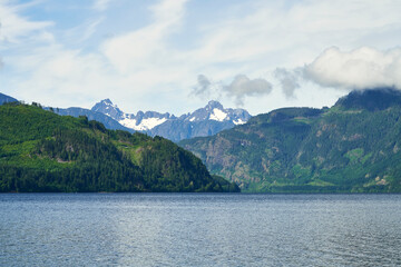View overlooking a lake to the distant recently logged mountains with fluffy clouds in the sky.