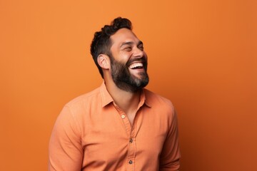 Obraz premium Portrait of a happy young bearded Indian man laughing against orange background