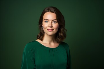 Fototapeta premium Portrait of a beautiful young brunette woman in a green dress on a dark green background