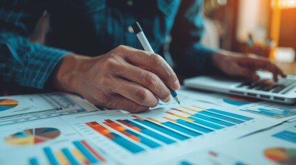 Fototapeta premium Close-up of a person analyzing financial charts and graphs on paper while using a laptop, representing business and data analysis concepts.