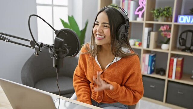A young hispanic woman sings joyfully in a radio studio, exuding beauty and confidence while recording a podcast.