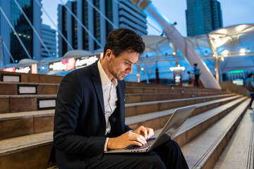 Caucasian young businessman sitting and work outdoor in city at night.