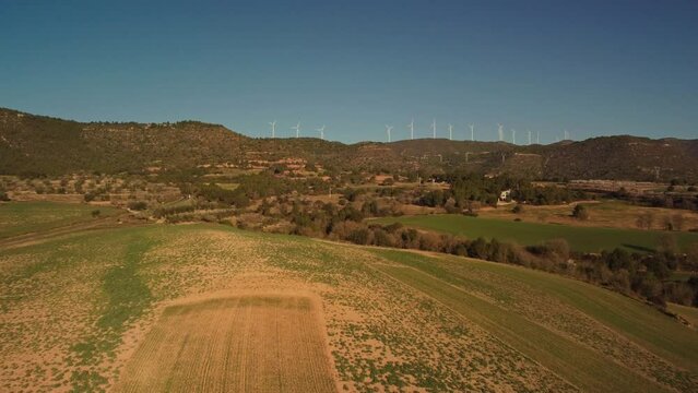 Windmills spinning in the distance over green and brown fields near Igualada, Barcelona