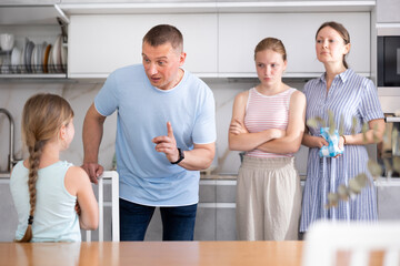 Fototapeta premium Preteen girl with long pigtail standing in home kitchen, listening to disapproving words of father, mother and older sister. Concept of tension and disagreement arising between generations