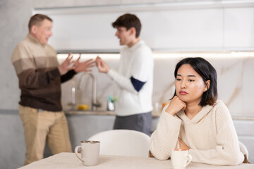 Obraz premium Young woman sad while sitting at table during family quarrel between adult and young man..