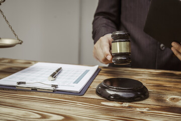 A businessman in a formal suit signs a contract, hands close up, suggesting possible bribery, at a wooden desk with legal documents, scales, and a wooden gavel representing legislation.