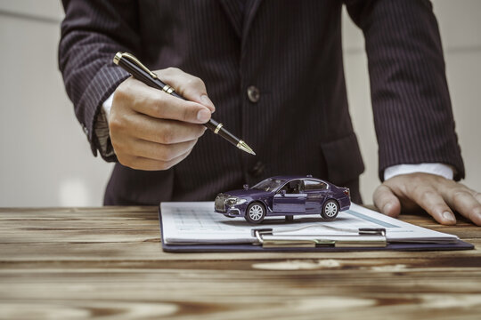 A businessman in a formal suit signs a contract, hands close up, highlighting financial terms like amortization, APR, and asset management, documents symbolizing various loan and insurance concepts.